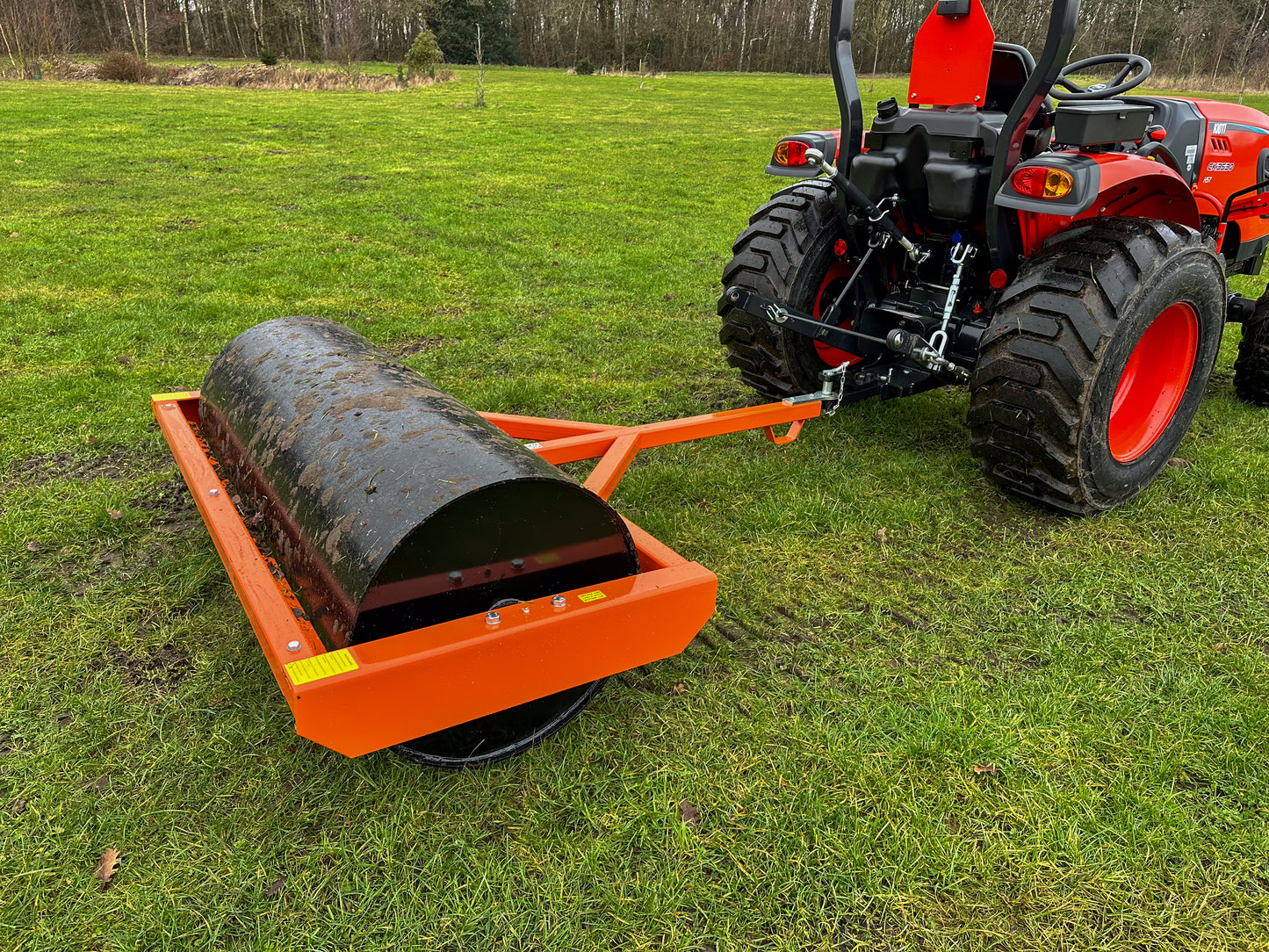 Red tractor pulling a FarmMaster tractor land roller on a grassy field