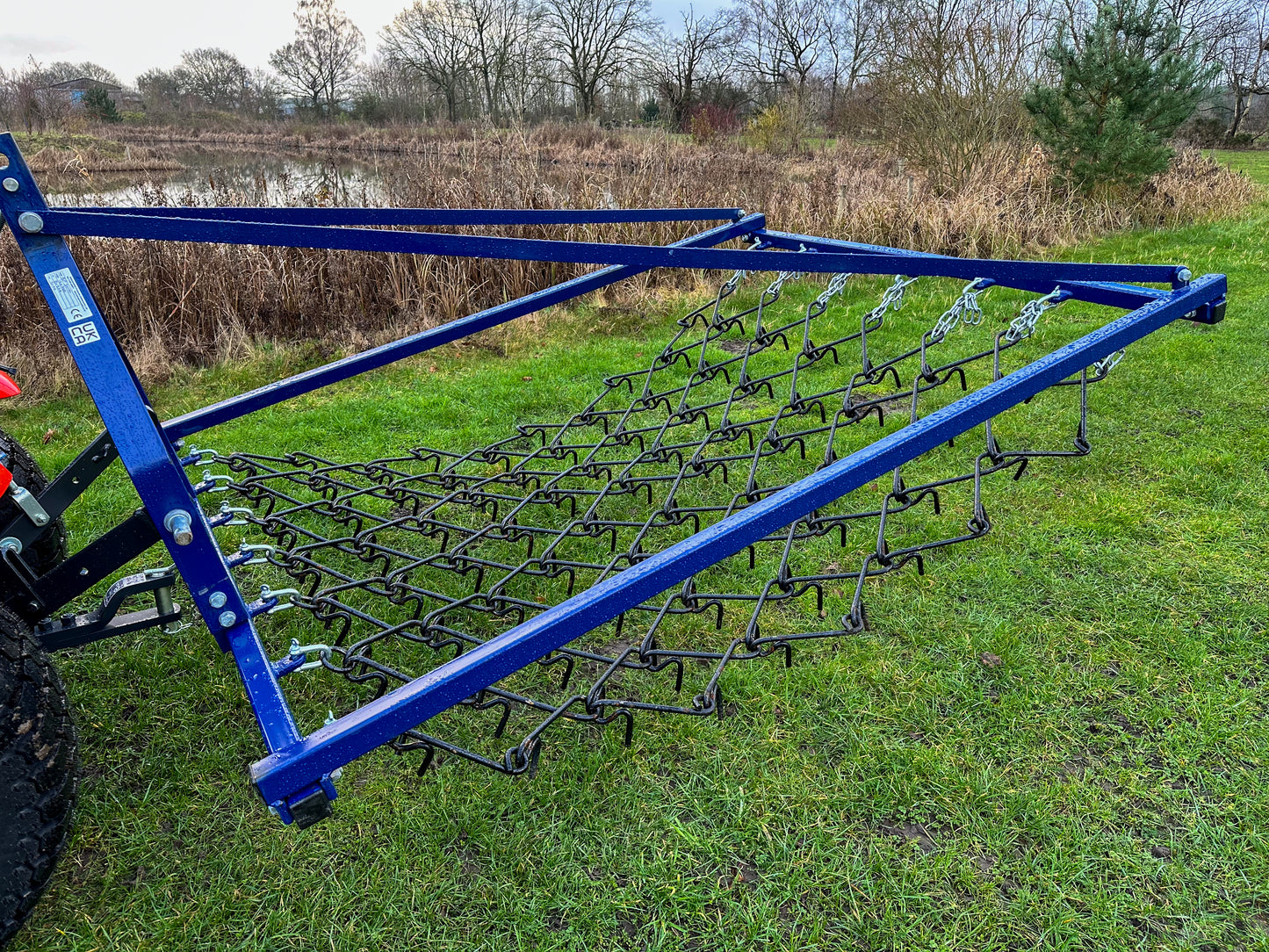 FarmMaster Framed Chain Harrow on a grassy field with a pond and trees in the background