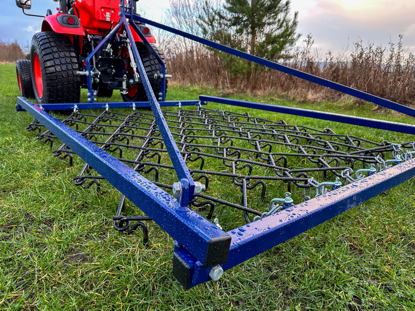 A tractor with a FarmMaster Framed Chain Harrow on a grassy field.