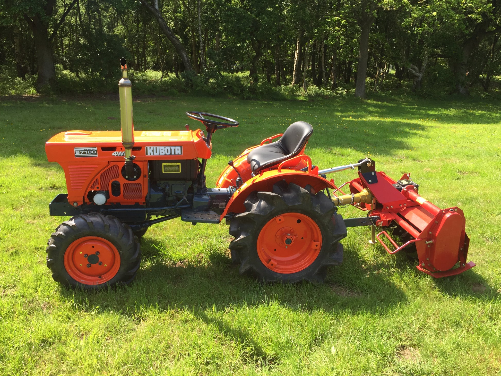 Orange Kubota tractor with aFarmMaster tractor rotavator on a grassy field.