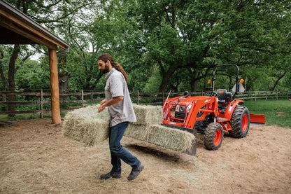 Man working with a Kioti tractor and hay in an outdoor setting