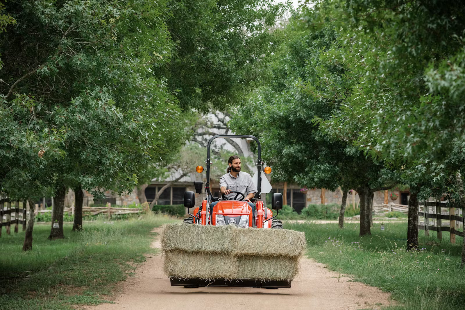 Person operating a Kioti compact tractor with a load of hay in a rural setting