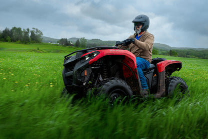 Person riding a red Can-Am ATV in a grassy field with a cloudy sky.