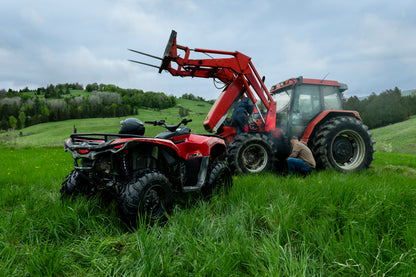 Red tractor with a front loader and a Can-Am ATV in a grassy field.