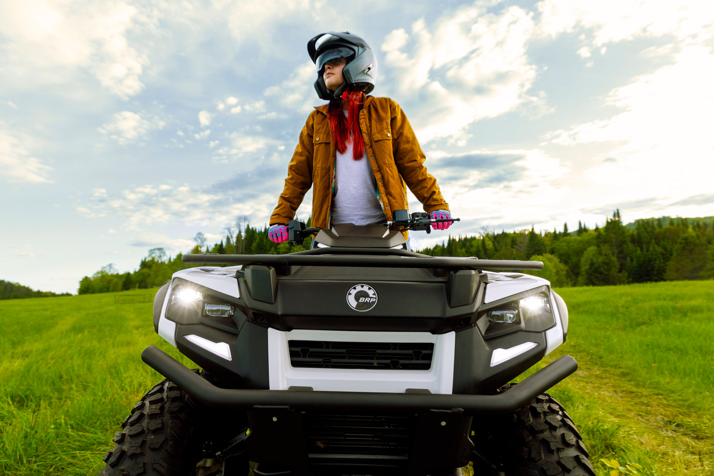 Person on a Can-Am ATV in a grassy field with a scenic background