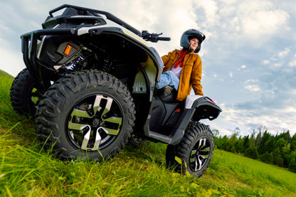 Person sitting on a Can-Am Outlander Electric ATV in a grassy outdoor setting with trees and sky in the background