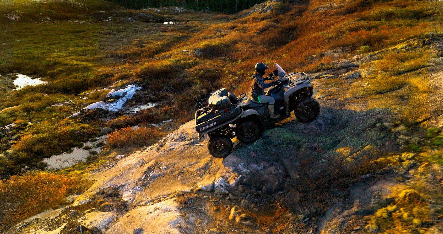 A Can-Am 6x6 ATV in a rugged, natural landscape with grass and rocks.