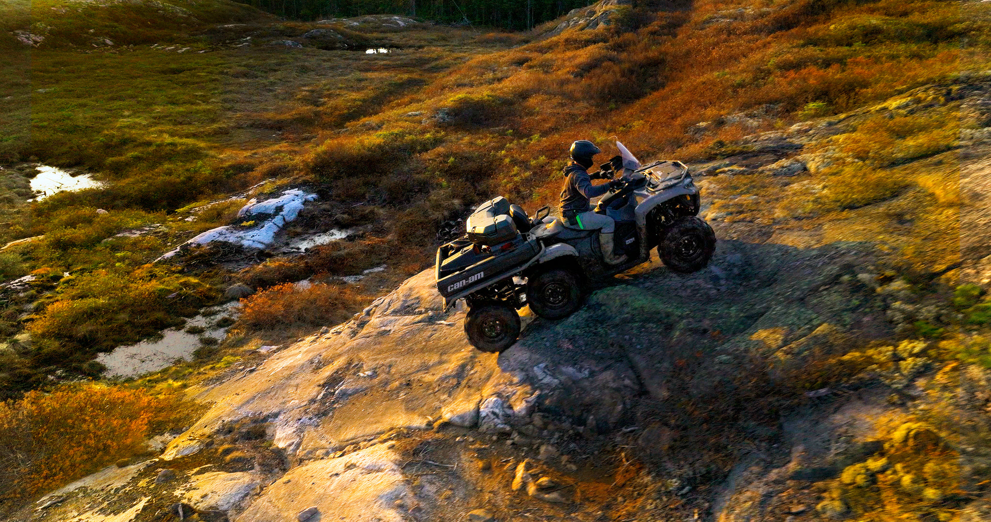 A Can-Am 6x6 ATV in a rugged, natural landscape with grass and rocks.