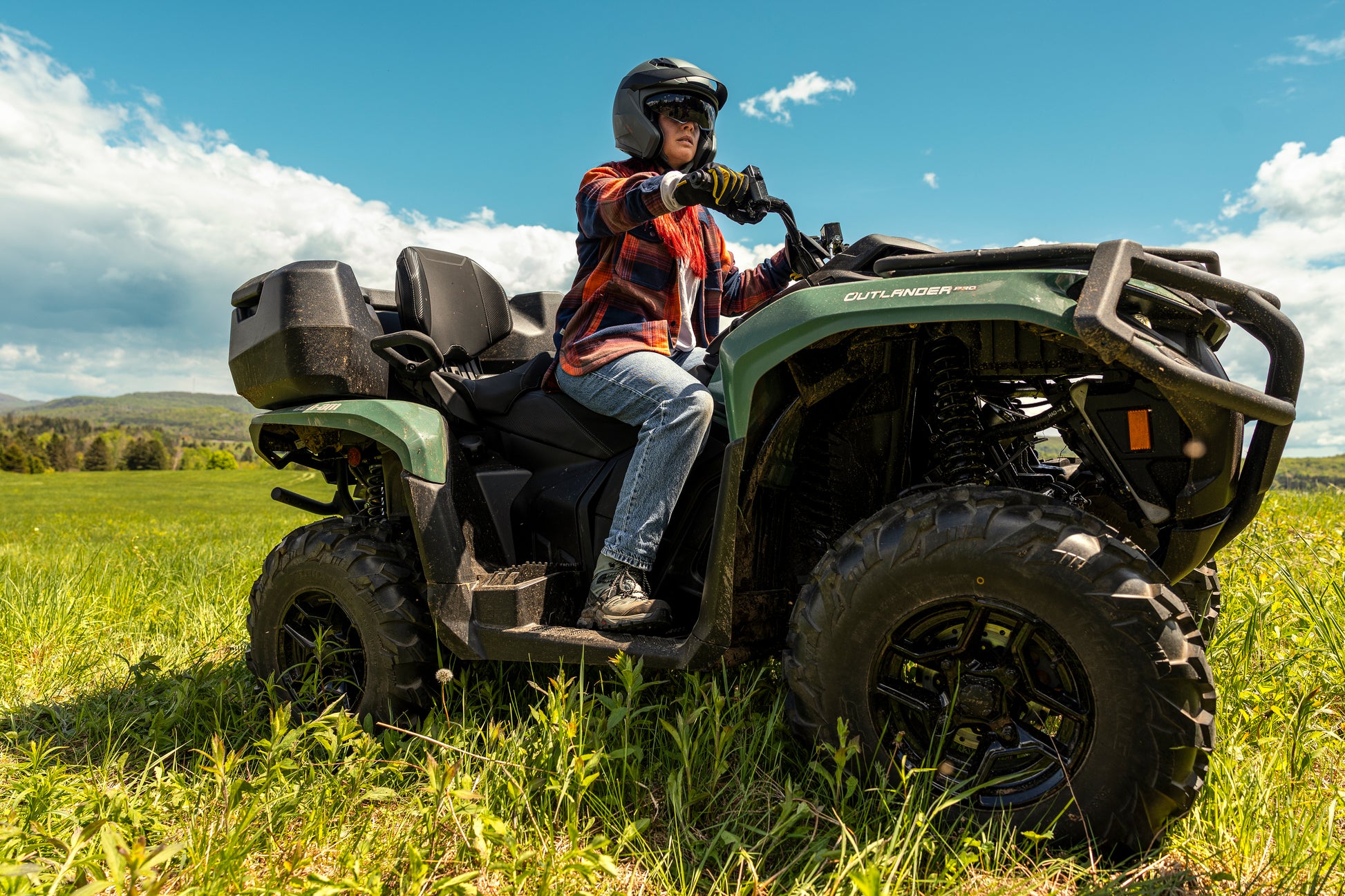 Person riding a Can-Am ATV in a grassy field with a clear sky