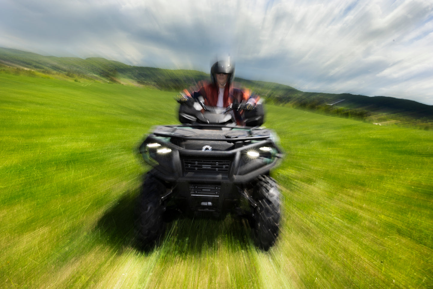 Person riding a Can-Am ATV on a grassy field with a scenic background