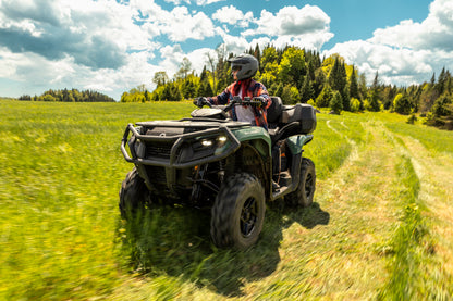 Person riding a Can-Am ATV on a grassy trail with trees in the background