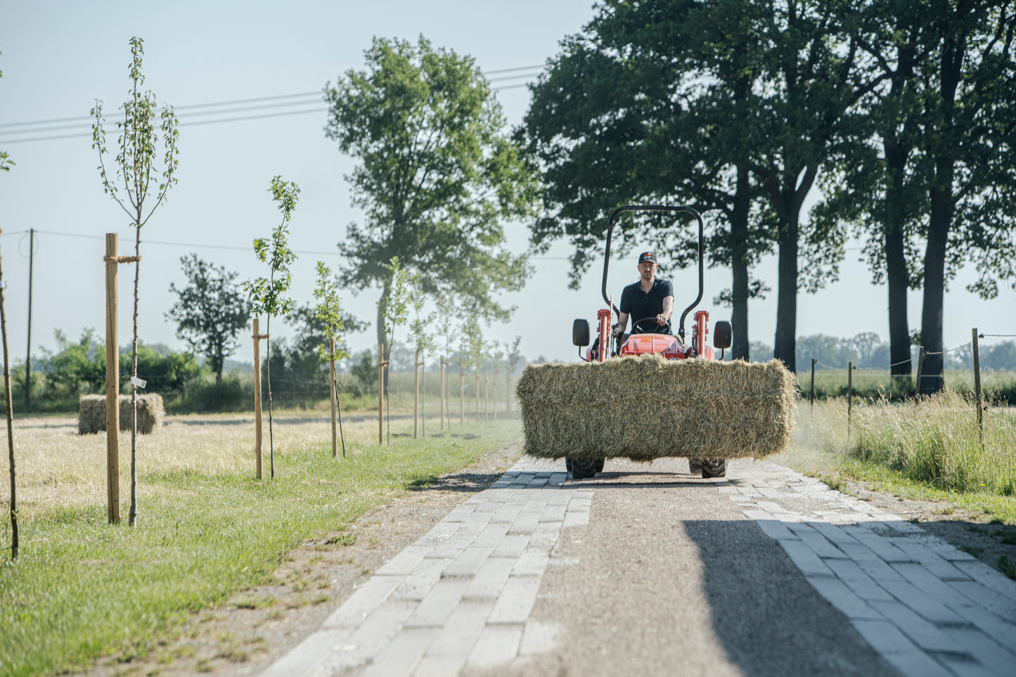 Person driving a Kioti tractor with hay bales on a rural road