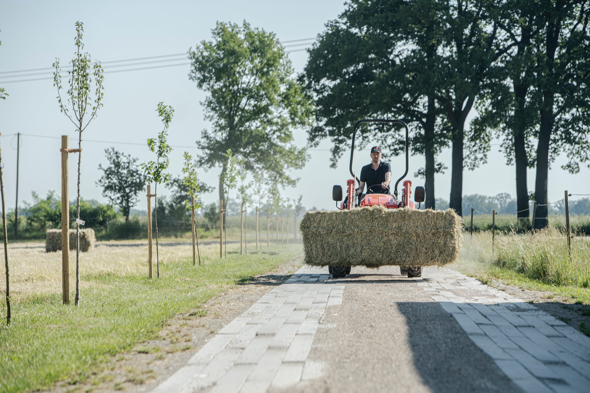 Person driving a Kioti tractor with hay bales on a rural road