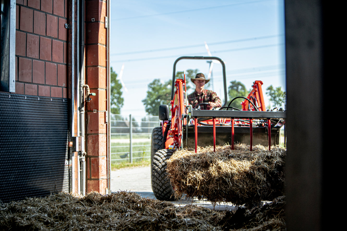 Person operating a Kioti tractor with hay bales in an open garage