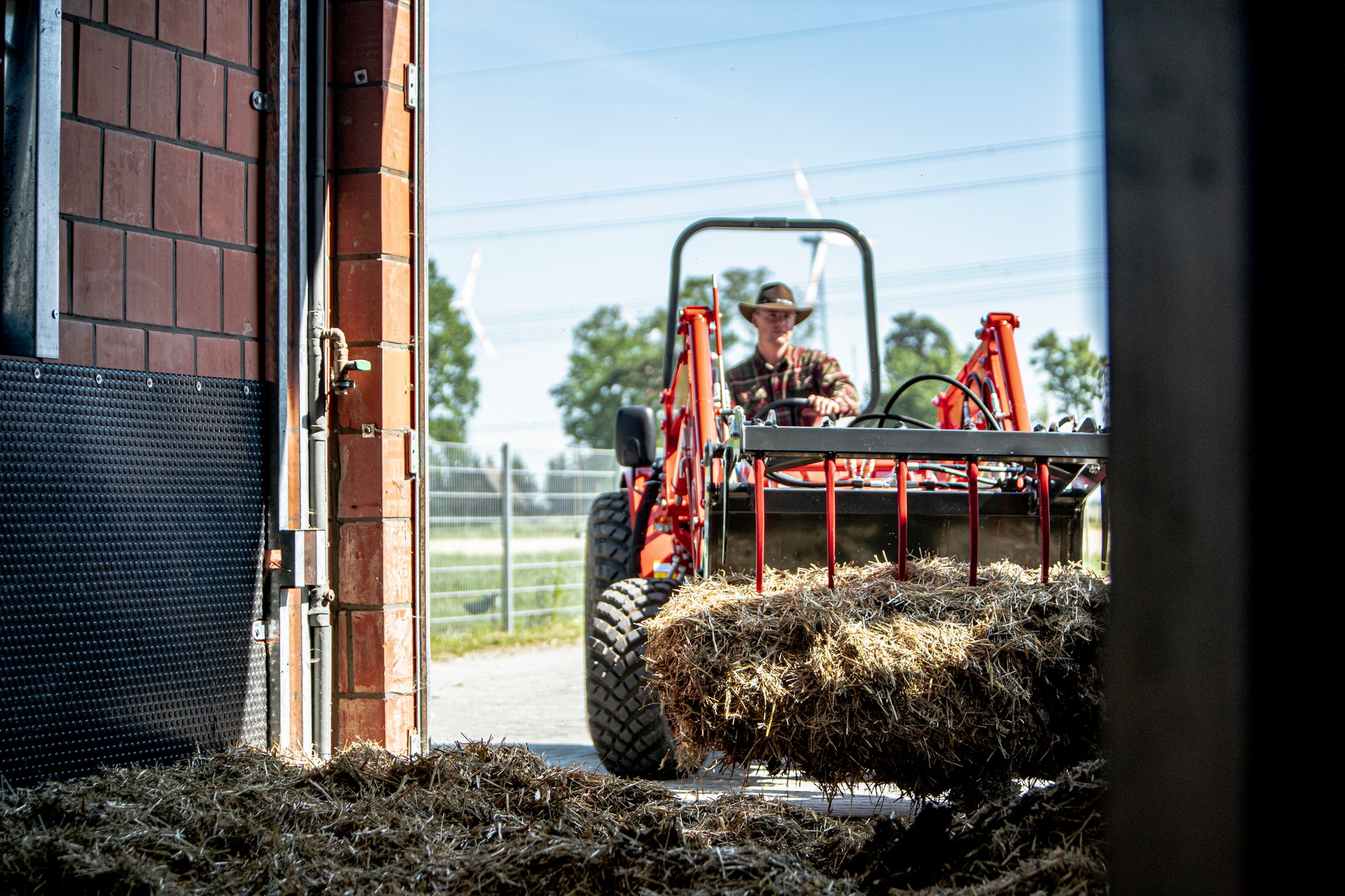 Person operating a Kioti tractor with hay bales in an open garage