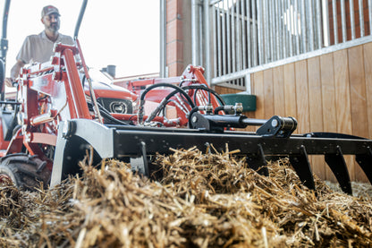Kioti Tractor plowing through straw with a person in the background
