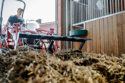 Person operating a Kioti tractor with a plow in a barn setting