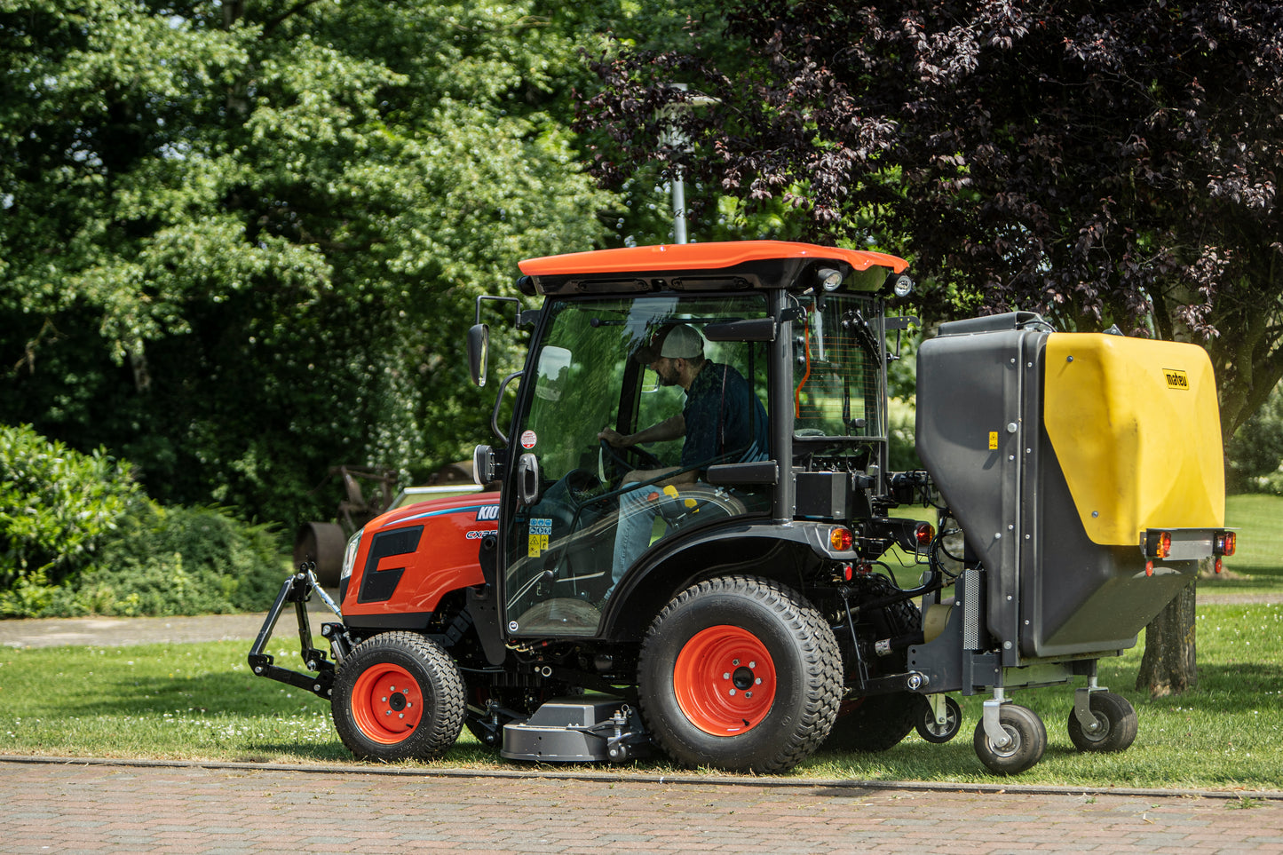 Kioti tractor with a collector attachment on a grassy area with trees in the background