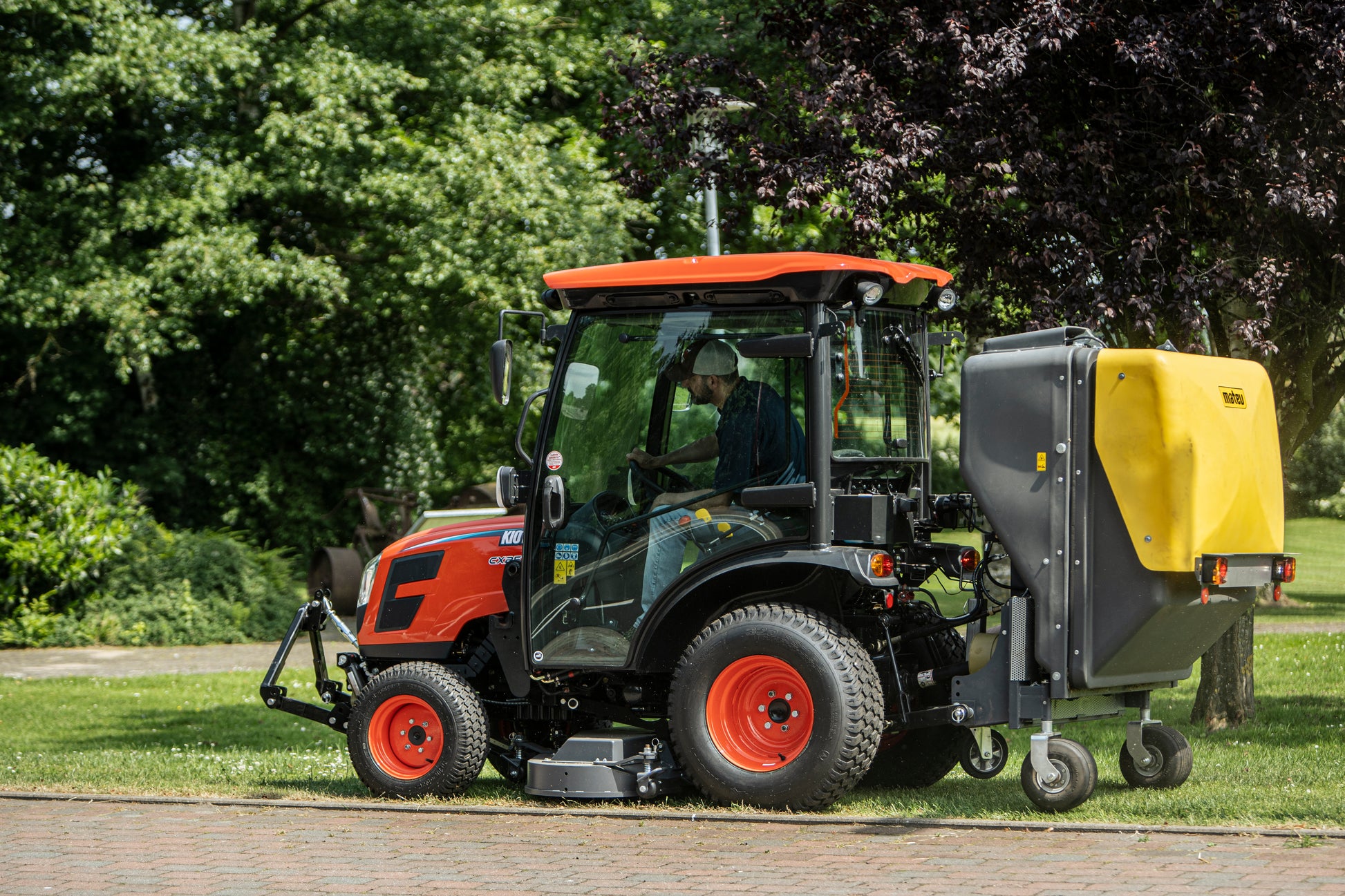 Kioti tractor with a collector attachment on a grassy area with trees in the background
