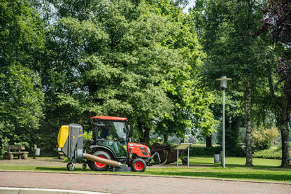 Small Kioti tractor with collector attachment on a road lined with trees