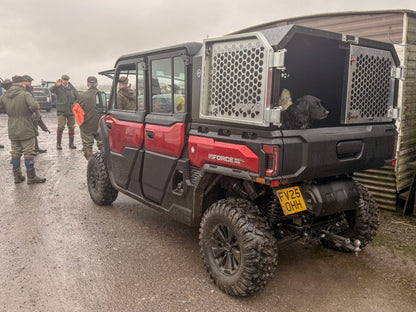 Red CFMOTO off-road vehicle with a dog crate on a muddy road, surrounded by people.