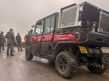 Red CFMOTO UFORCE U10 Pro XL off-road vehicle with a cage on the back, surrounded by people and dogs in a field.