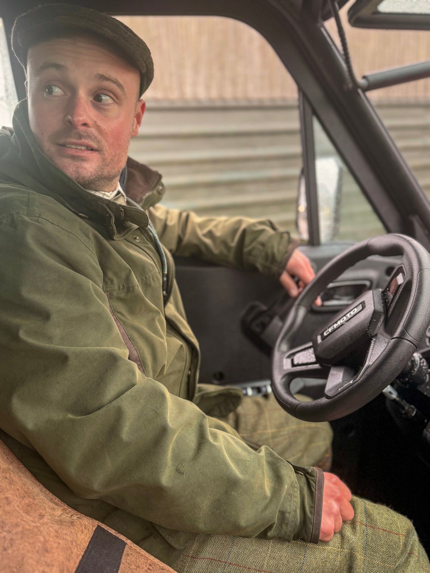 Man sitting inside a CFMOTO vehicle wearing a green jacket and cap.