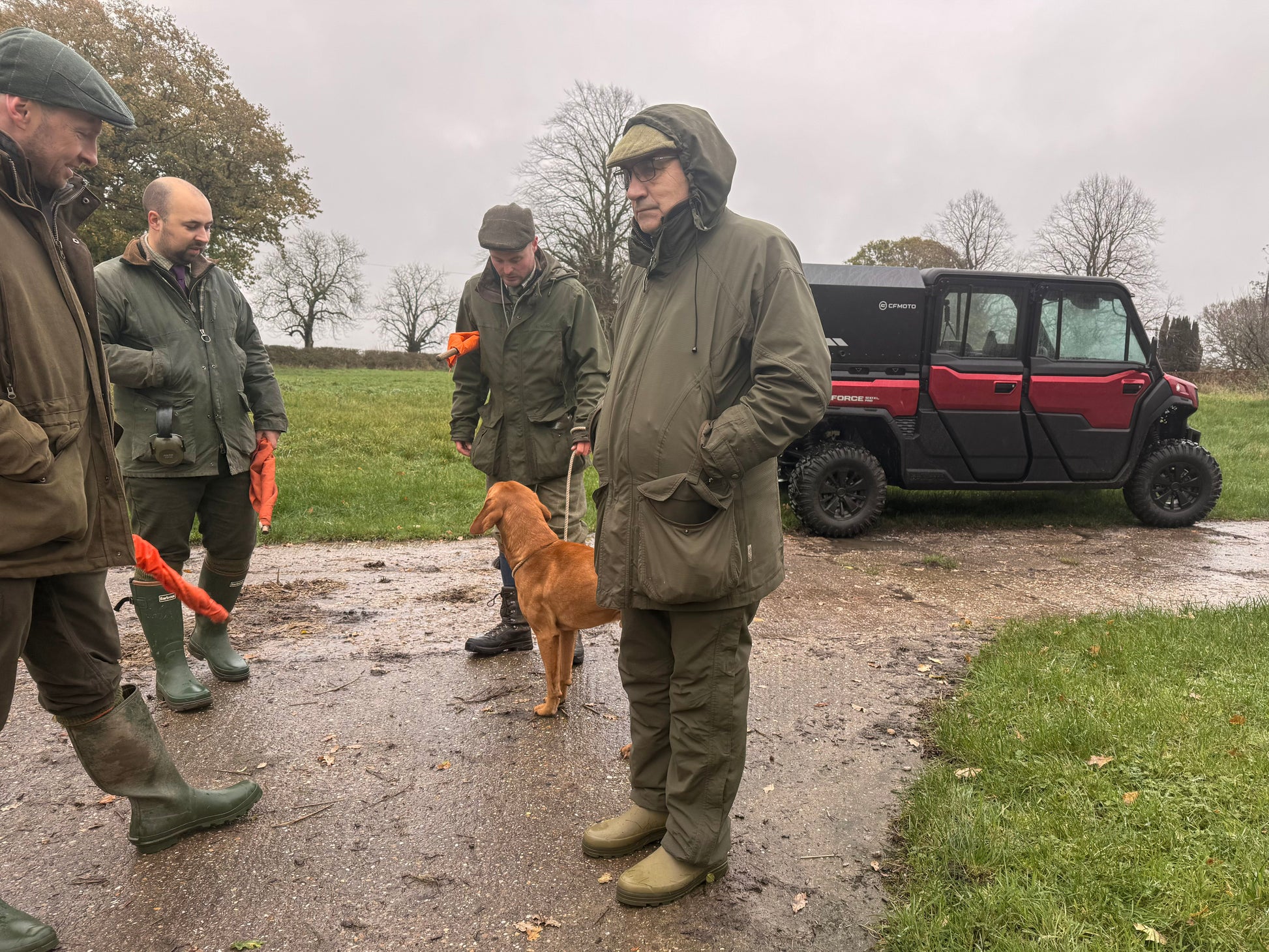 Four men in outdoor gear with a dog on a muddy path, near a CFMOTO UTV