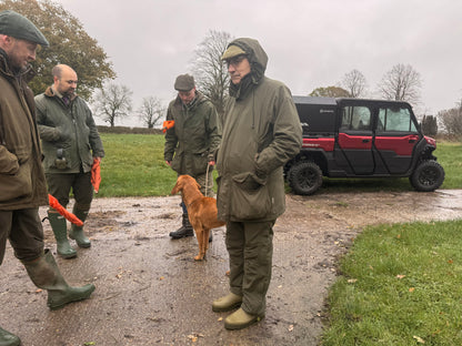 Four men in outdoor gear with a dog on a muddy path, near a CFMOTO UTV