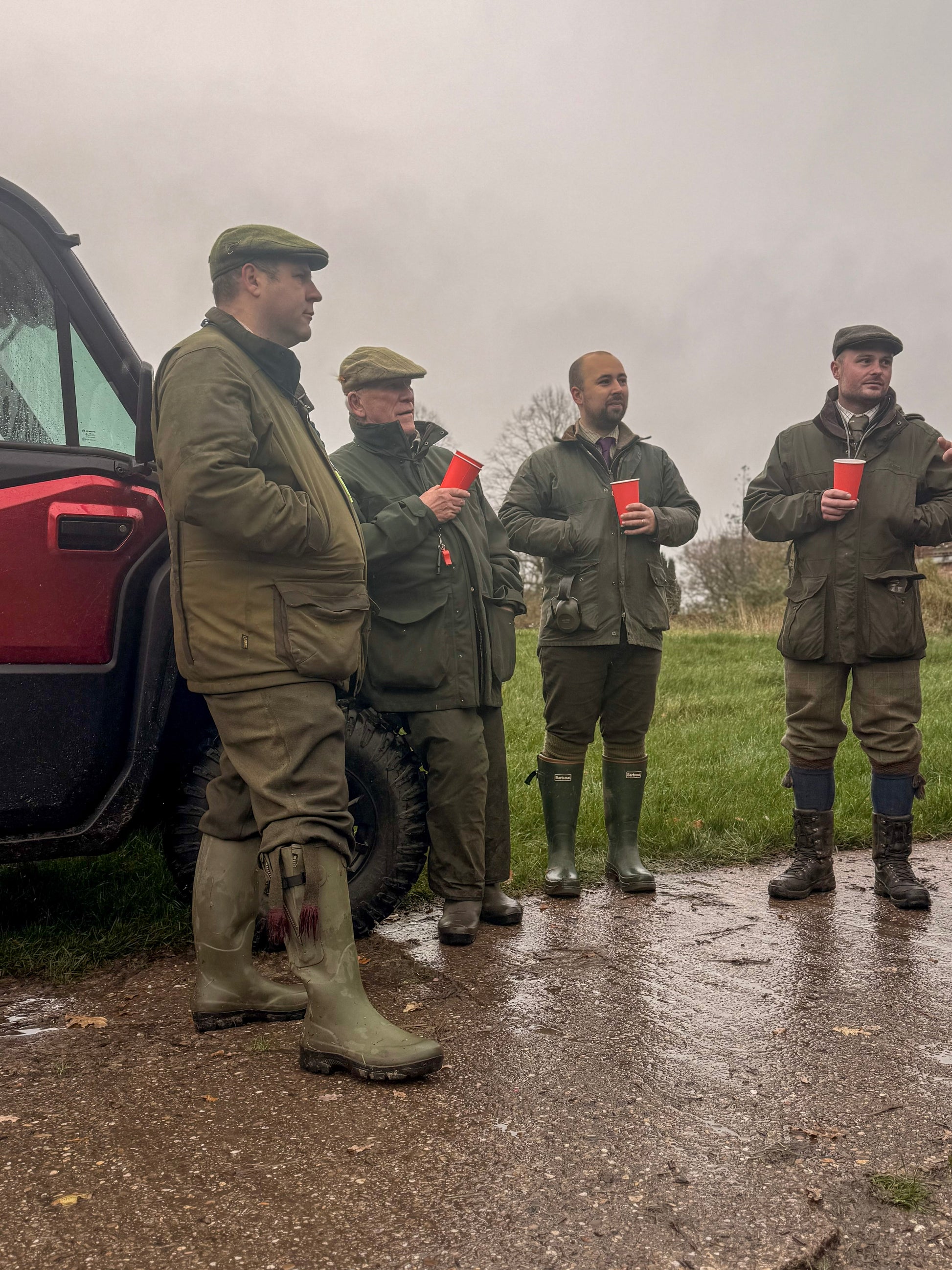 Four men in green hunting gear standing near a CFMOTO UFORCE U10 Pro XL on a wet road.