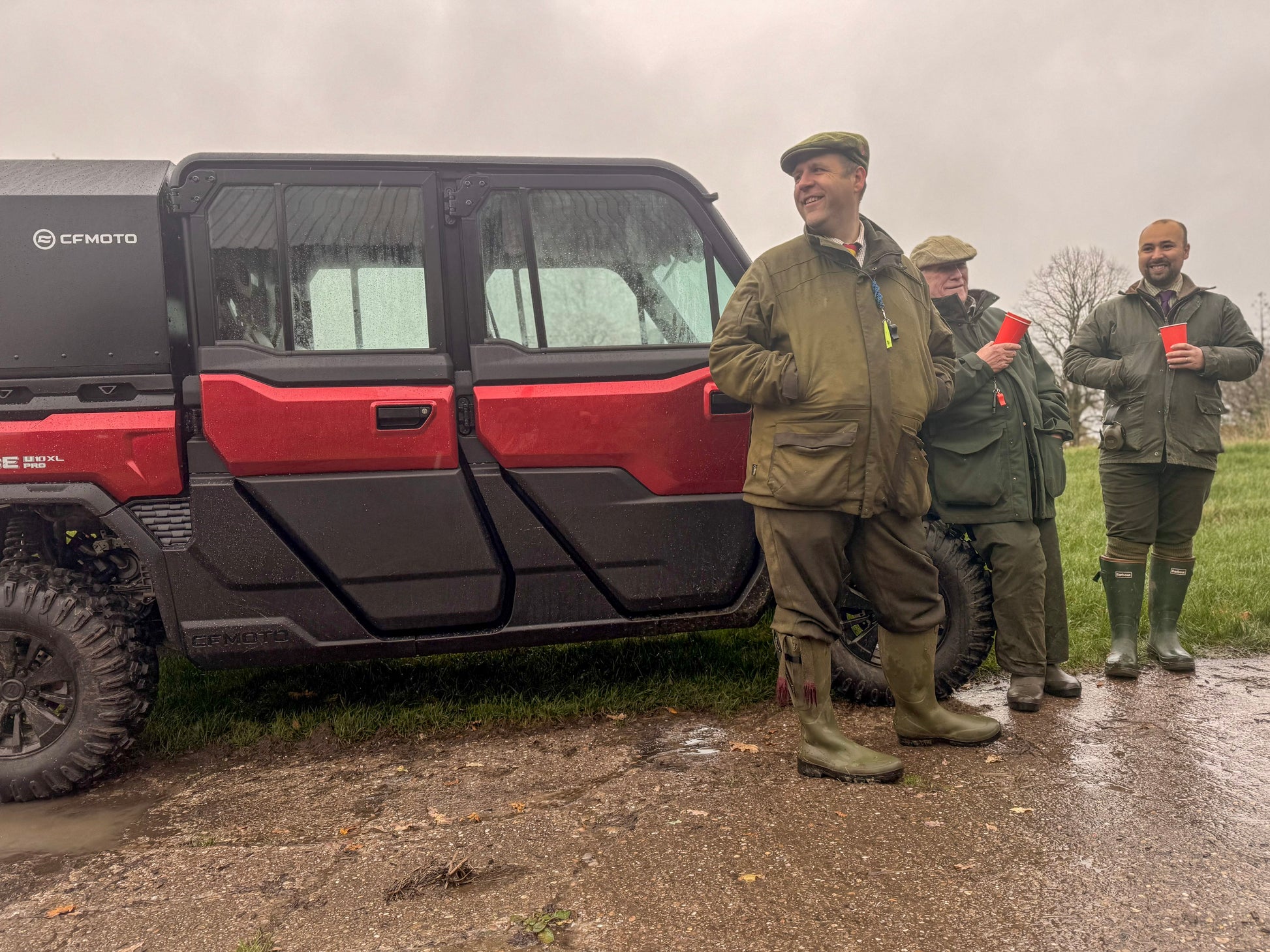 Three men in outdoor gear standing next to a red CFMOTO UFORCE U10 Pro XL on a rainy day.