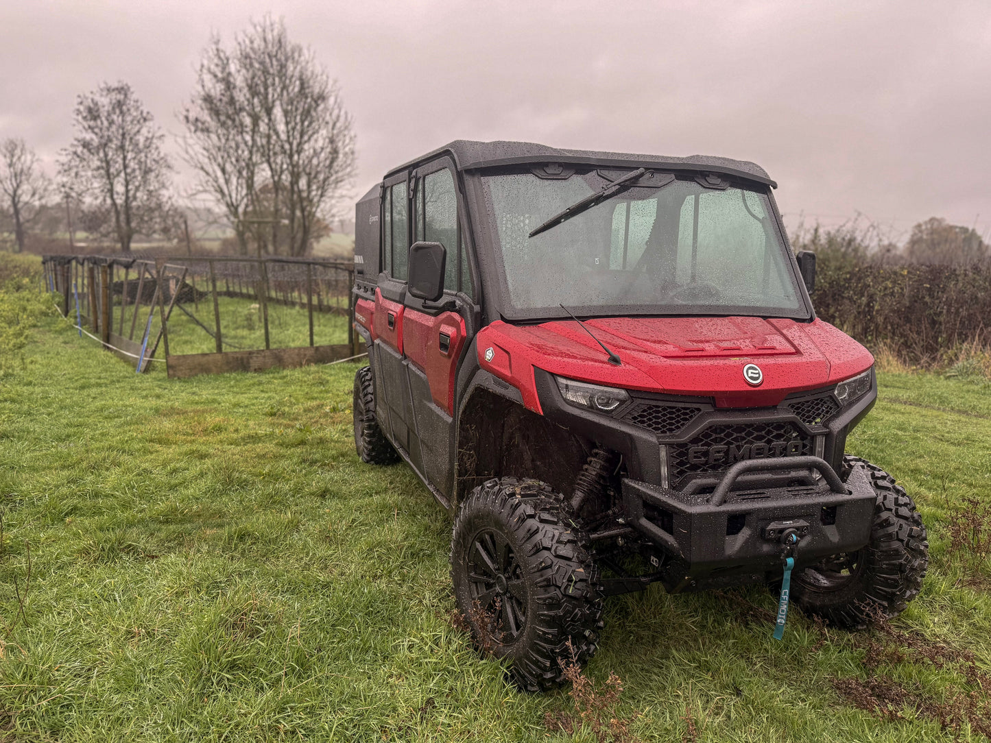 Red CFMOTO utility vehicle parked on grass with a cloudy sky