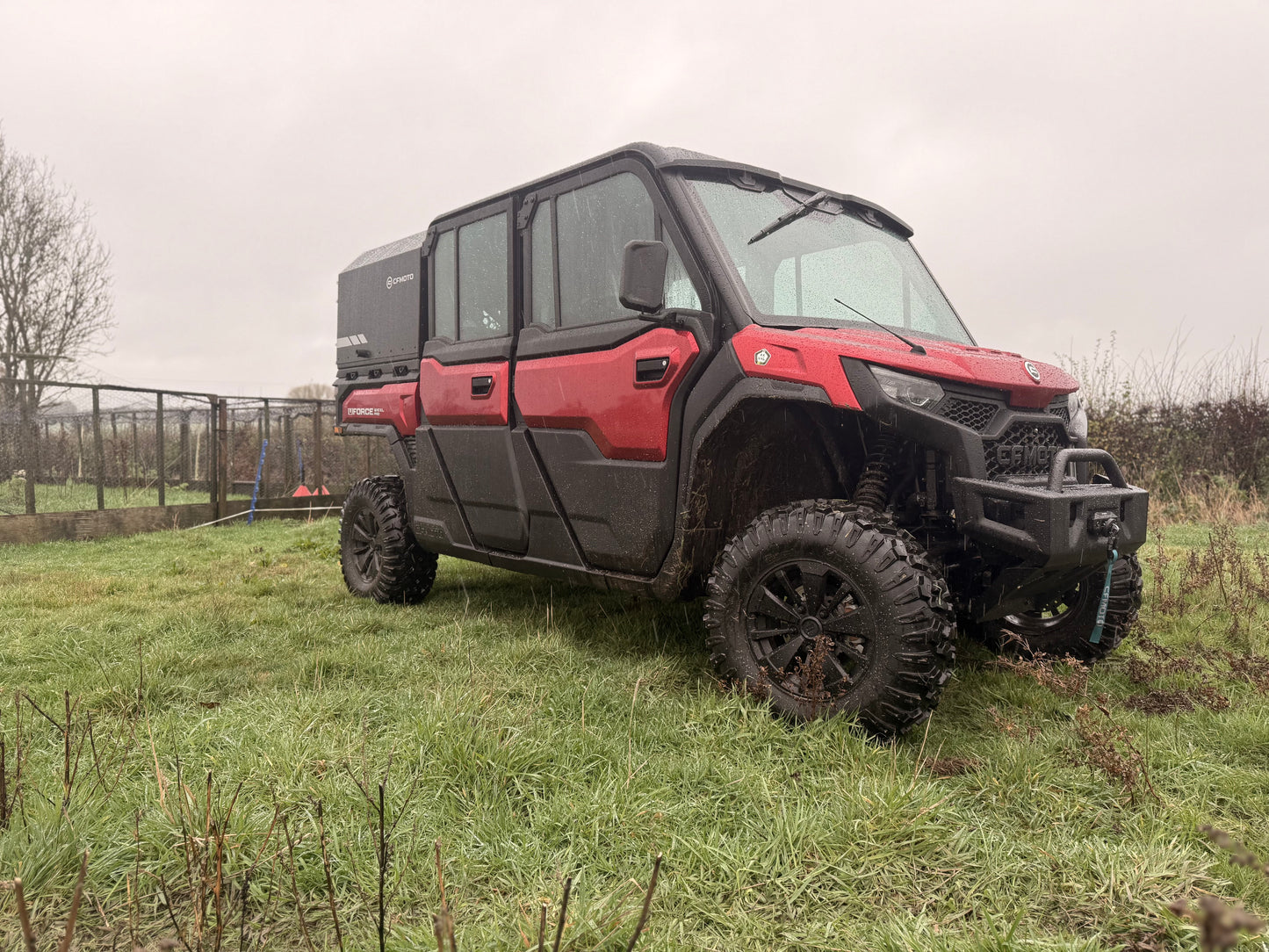 Red CFMOTO off-road vehicle in a grassy field with a cloudy sky.