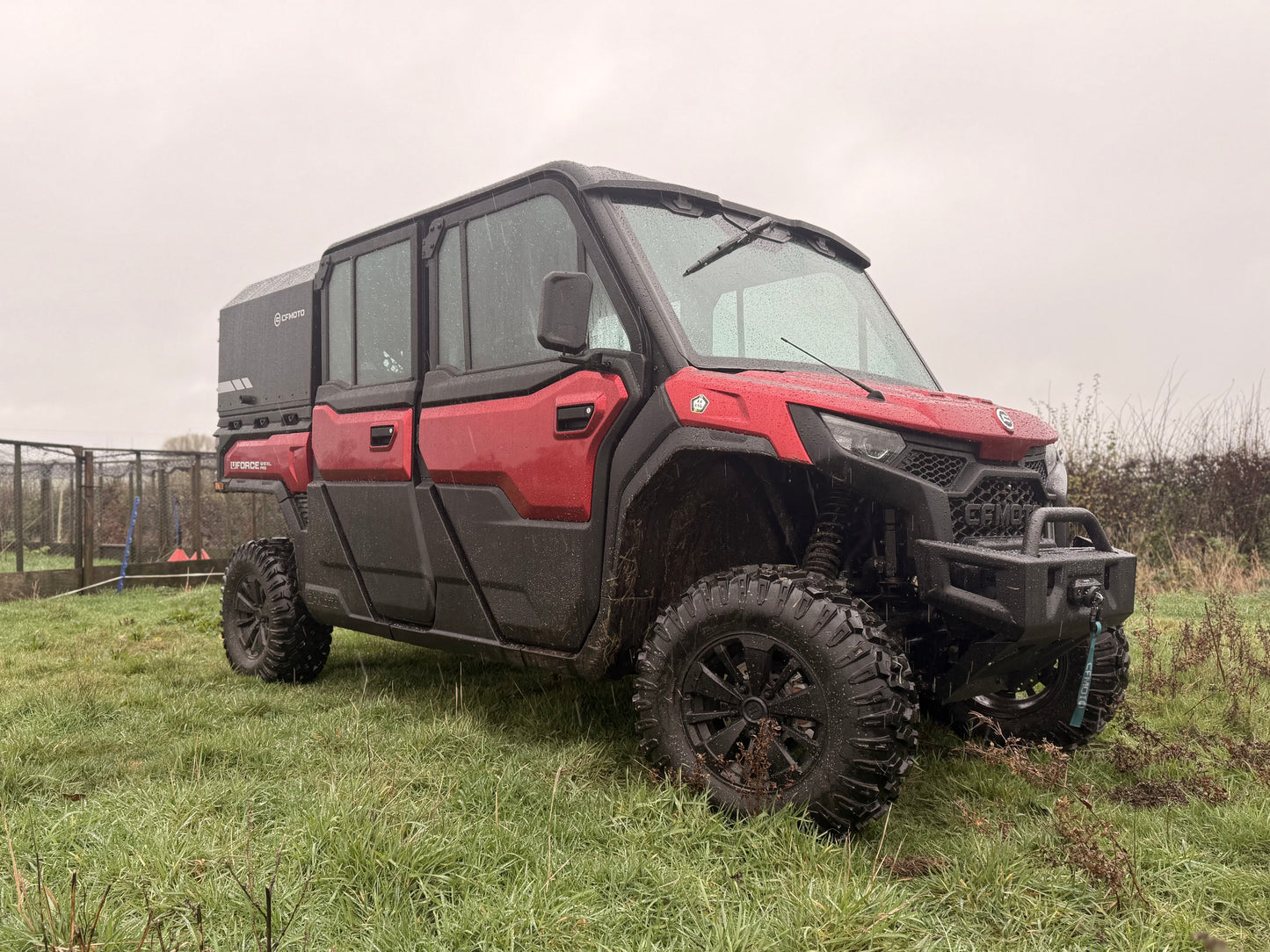 Red CFMOTO utility vehicle parked on grass with a cloudy sky.