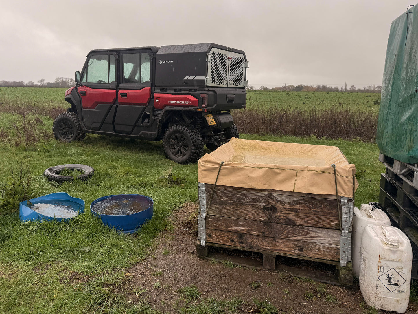 CFMOTO vehicle parked in a field with a wooden crate and water containers nearby.