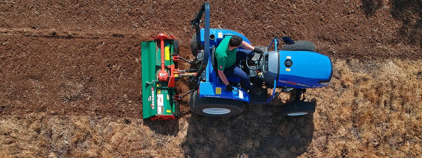 Person operating a blue tractor and Wessex tractor rotavator in a field