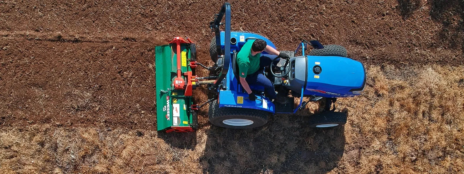 Person operating a blue tractor and Wessex tractor rotavator in a field