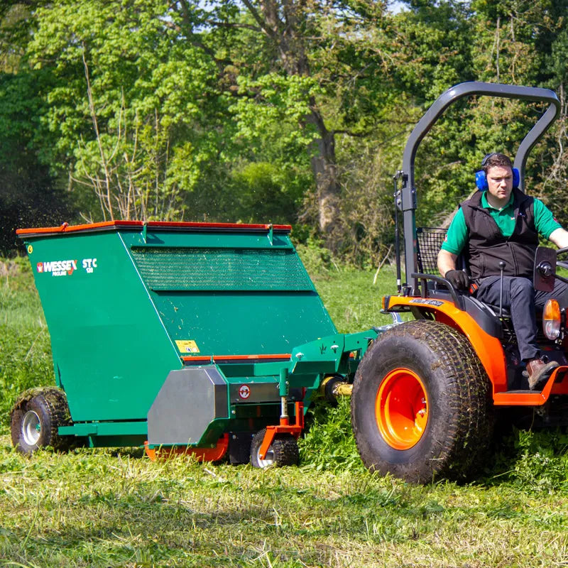 Person operating a tractor with a Wessex flail collector in a grassy field.