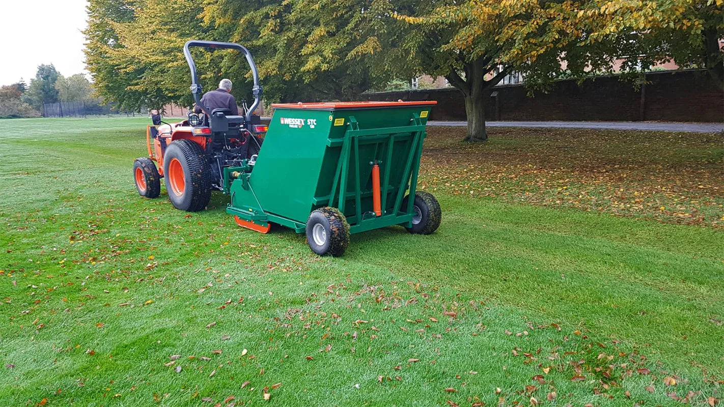 Person operating a tractor with a Wessex flail collector on a grassy field.