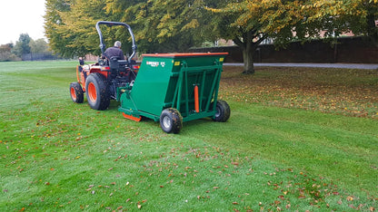 Person operating a tractor with a Wessex flail collector on a grassy field.