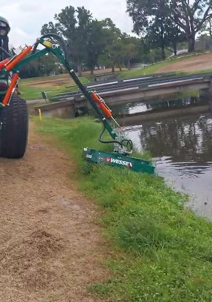 Tractor with a Wessex hedge cutter attachment near a body of water