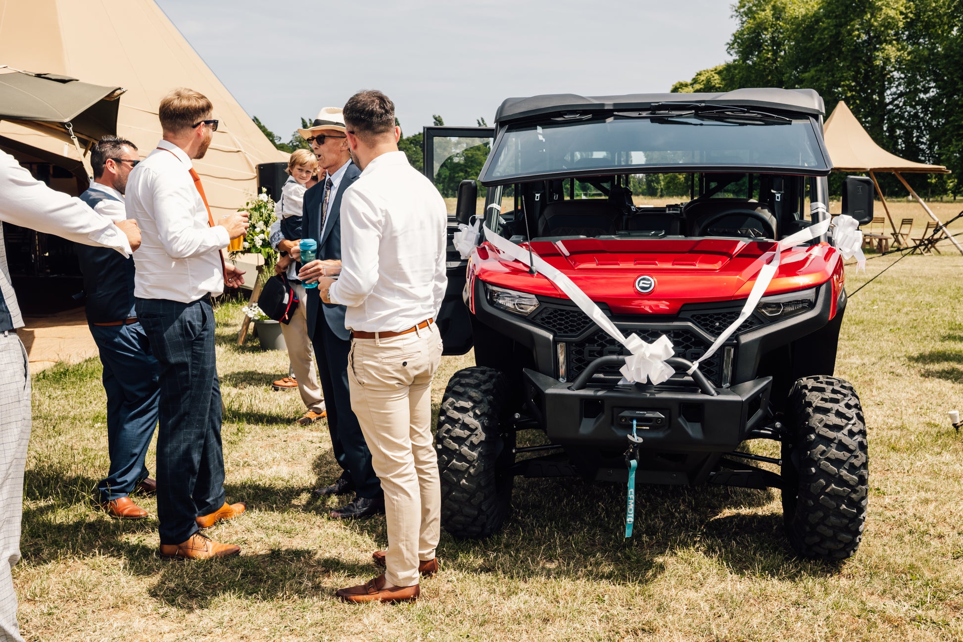 Red CFMOTO UTV off-road vehicle with a white ribbon at an outdoor wedding.