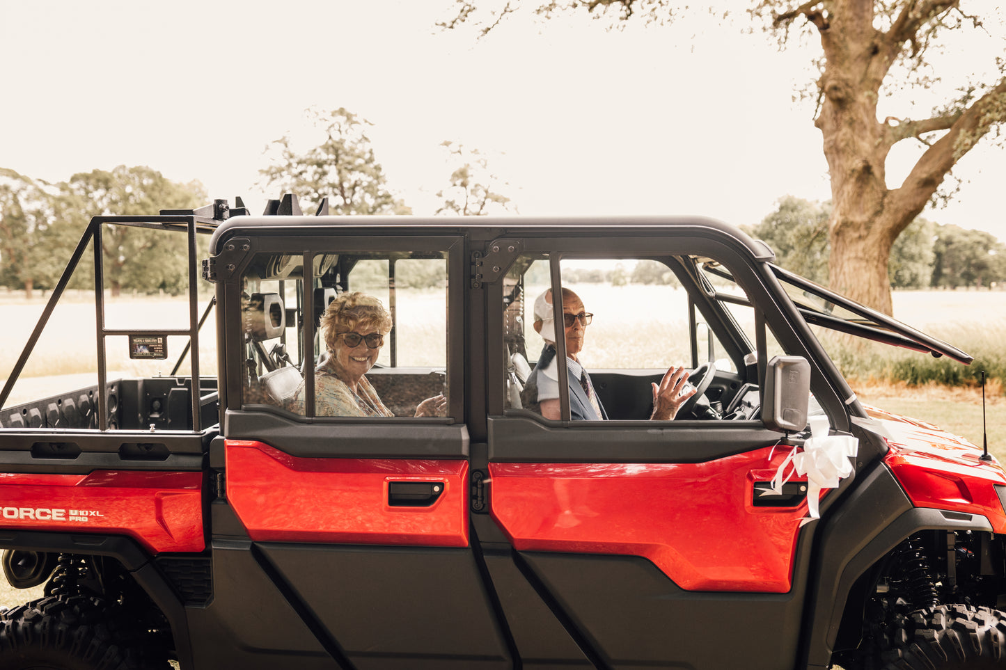 Red CFMOTO off-road vehicle with two people inside, surrounded by trees and open space.