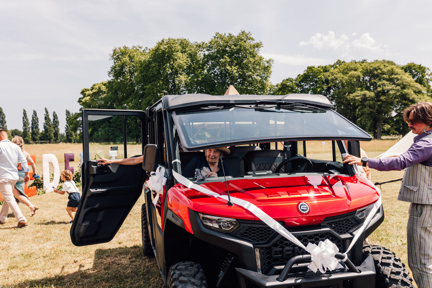 Red CFMOTO UFORCE U10 Pro XL off-road vehicle with open door at a wedding with people around