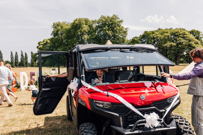 Red CFMOTO UFORCE U10 Pro XL off-road vehicle with open door at a wedding with people around
