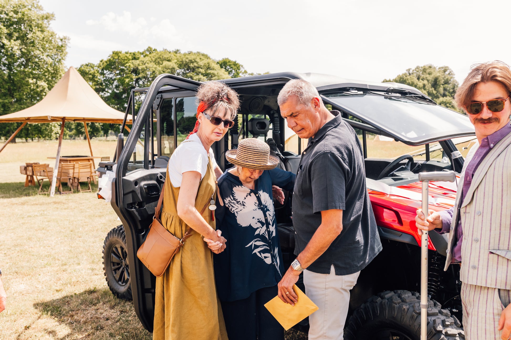Group of people standing near a CFMOTO UFORCE U10 Pro XL with trees and a tent in the background.