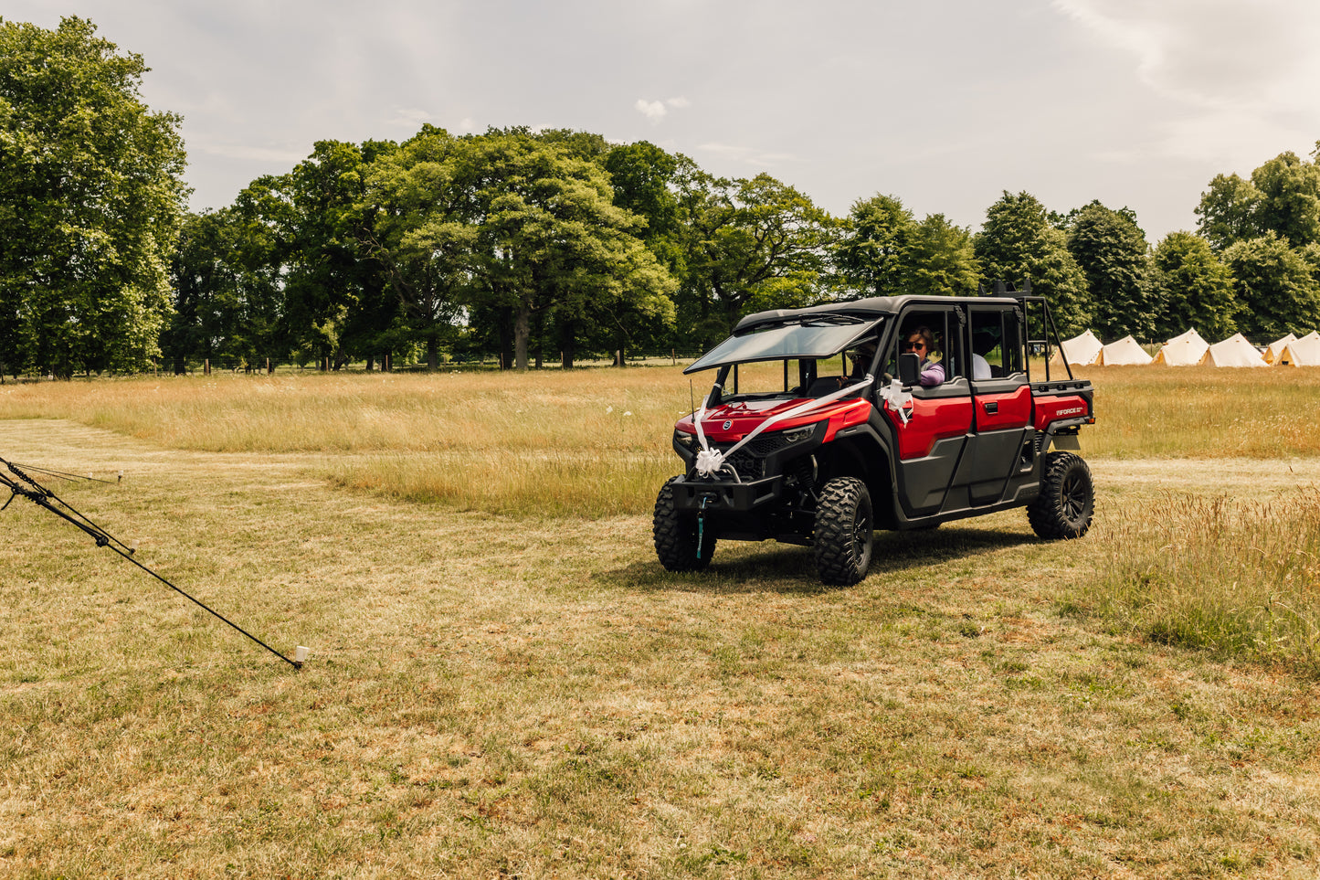 Red CFMOTO UFORCE U10 Pro XL off-road vehicle in a field with trees and tents in the background