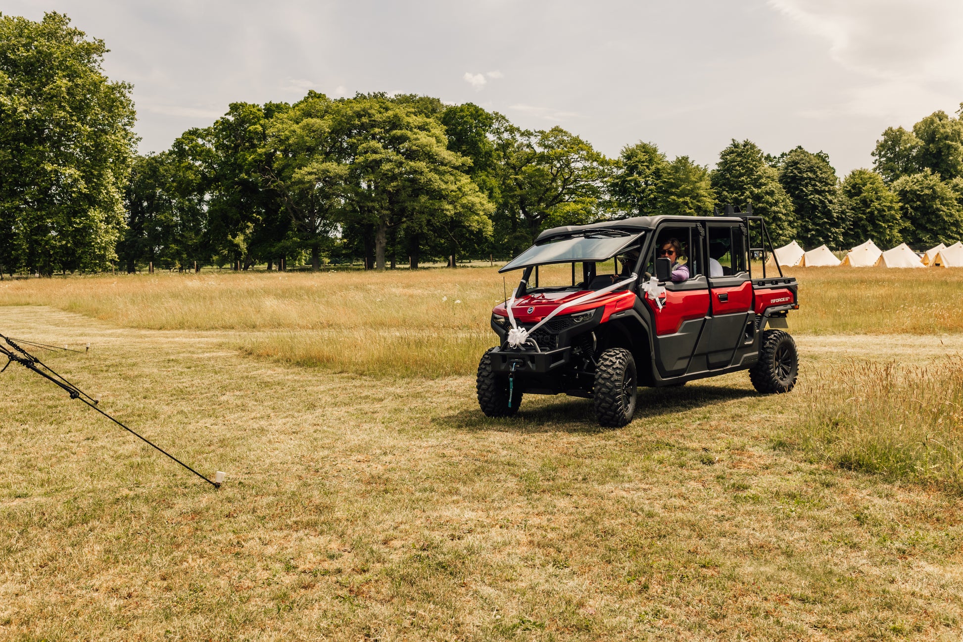 Red CFMOTO UFORCE U10 Pro XL off-road vehicle in a field with trees and tents in the background