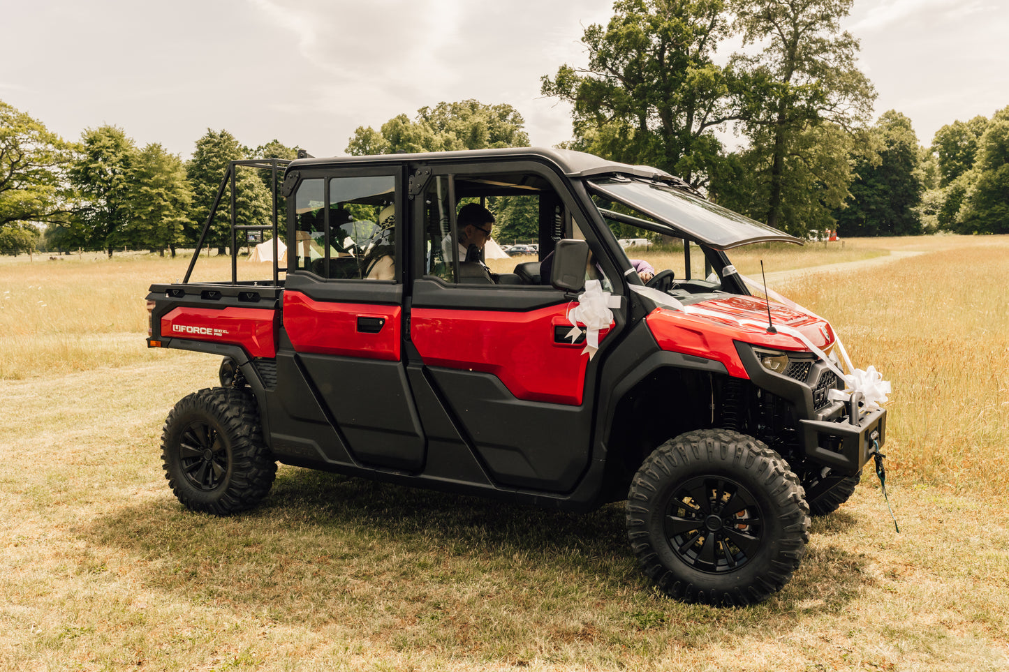 Red CFMOTO utility vehicle parked on a grassy field with trees in the background