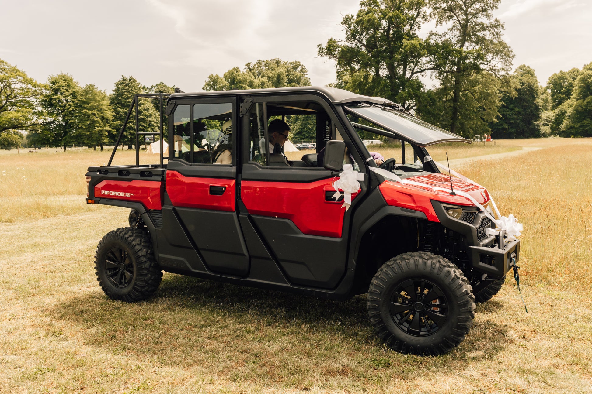 Red CFMOTO utility vehicle parked on a grassy field with trees in the background